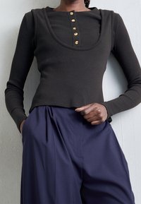 Dunkel gestreiftes Langarmoberteil mit weitem Ausschnitt und fünf goldenen Knöpfen, kombiniert mit hochgeschnittenen navyblauen Hosen.