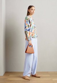 Blusa floreale multicolore, pantaloni a gamba larga blu chiaro, scarpe flat beige e una piccola borsa triangolare marrone.