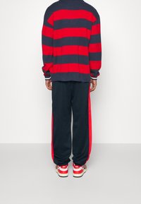 Suéter de rayas rojas y marino con un corte relajado, combinado con pantalones de chándal marinos con rayas laterales rojas y zapatillas rojas.