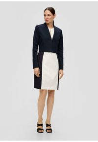 Marineblauwe cropped blazer met V-hals, gecombineerd met een wit en marineblauw gekleurd blokjurk. De outfit heeft een strak, gestructureerd design en hakken met enkelbandje.