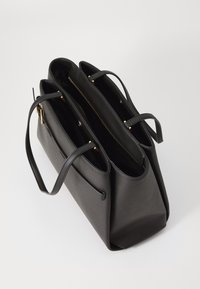 Black leather tote bag with two open compartments, gold zipper, and dual handles. Features a textured surface and structured shape.