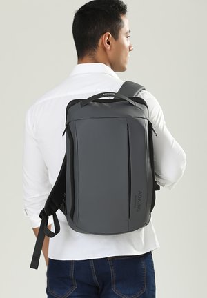 Grijze rugzak met een slank ontwerp, voorzien van een bovenhandvat, verstelbare schouderbanden, voorste ritszakken en een soepele, matte afwerking.
