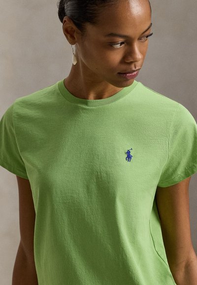 Πράσινη βαμβακερή μπλούζα με στρογγυλή λαιμόκοψη, κοντά μανίκια και μικρό μπλε κεντημένο λογότυπο στο στήθος. Λείο υφή.