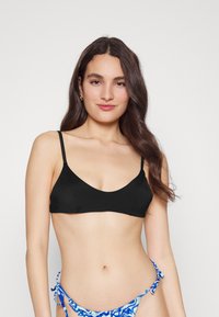 Top de biquíni preto com alças finas, design em V profundo e textura suave. Acompanha um fundo de biquíni azul com padrões e laços.