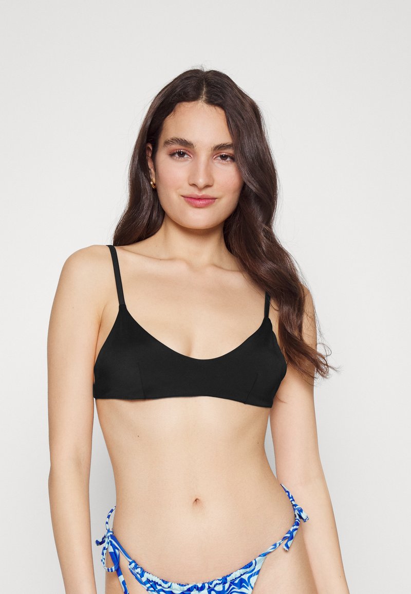 Top de biquíni preto com alças finas, design em V profundo e textura suave. Acompanha um fundo de biquíni azul com padrões e laços.