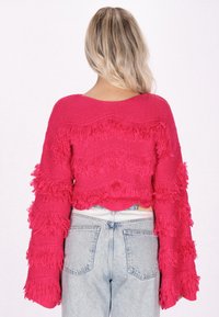 Rosa stickad kort tröja med volangfransdetaljer på ärmar och kropp, med en vid halsringning och en avslappnad passform.