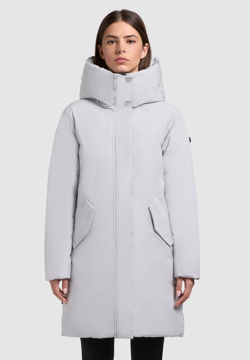 Šviesiai pilka pūkinė striukė su aukštu apykakle, priekyje užsegama spaustukais ir dviem šoninėmis kišenėmis. Lygi tekstūra su šiek tiek blizgiu paviršiumi.