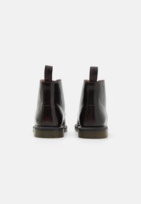 Schwarze Lederknöchelstiefel mit glänzender Oberfläche, kontrastierenden roten Nähten und Ziehlaschen an der Rückseite. Strukturierten Gummisohlen.