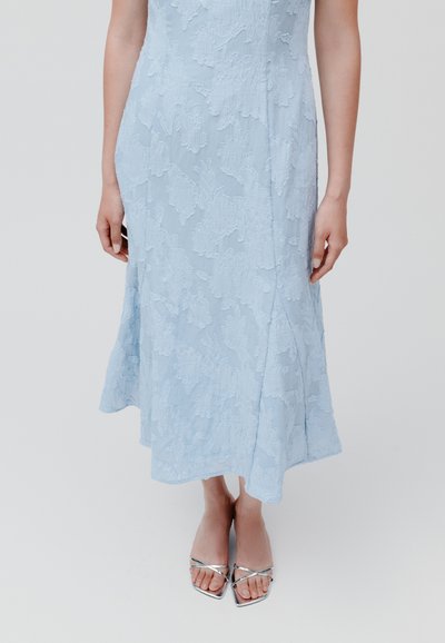 Himmelblaues Kleid mit strukturiertem Blumenmuster, in mittellanger Form, figurbetontem Oberteil und ausgestellt geschnittenem Saum. Begleitet von silbernen Schuhen mit quadrater Zehenform.