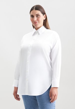 Hvid skjorte med knapper og spidse krave, lange ærmer og buet kant. Stoffet ser glat ud med en let glans.