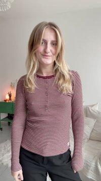 Bordo un sloksnes piedurkņu tops, kas izgatavots no ribota auduma, ar apaļu dekoltē un pieguļošu piegriezumu. Melni bikses papildina apģērbu.