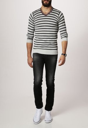 Pull en rayures grises et blanches avec un col en V et des poignets côtelés, associé à un jean noir et des baskets blanches. Coupe décontractée, texture en maille.