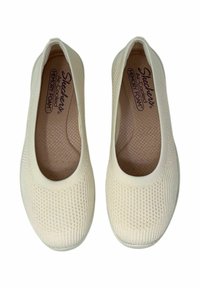 Un paio di scarpe slip-on beige di Skechers con texture a maglia e soletti in memory foam, mostrati dall'alto su uno sfondo bianco.