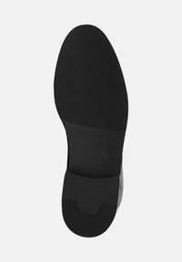 Suola di scarpa nera con texture liscia e scanalature per una migliore aderenza. Il design è curvato e affusolato verso la punta, con marchio in rilievo.