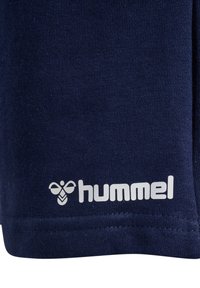 Dunkelblauer Baumwollstoff mit glatter Textur, versehen mit einem weißen Logo-Etikett mit einem Bienenmotiv und dem Wort "hummel" am Saum.