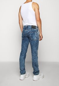 Niebieskie dżinsy z teksturowanym, bąbelkowym wzorem, pięcioma kieszeniami i czarną metką z tyłu. Noszone z białym topem na ramiączkach i białymi sneakersami.