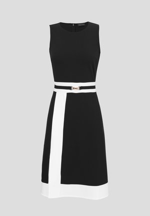 Αμάνικο μαύρο φόρεμα με λευκή κάθετη λωρίδα και στρίφωμα, με λευκή ζώνη με χρυσή αγκράφα στη μέση, σε γκρι φόντο.