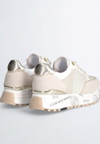 Sneaker beige e bianche con tomaia in suede e mesh, accenti metallici e suola testurizzata con dettagli del marchio vicino al tallone.