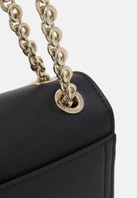 Černá kožená taška s pozlaceným řetízkovým popruhem, kulatým kováním, hladkou texturou a čistým, strukturovaným tvarem.