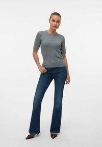 Grijze geribbelde korte mouwen trui, gecombineerd met donkerblauwe flared jeans en bruine puntige hakken met decoratieve accenten.