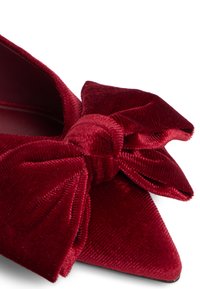 Røde flade sko i velvet med en stor sløjfe detalje foran, der har en glat overflade og et spidst tå-design.