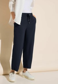 Mörkblå, lätta, byxor med elastisk midja, sidofickor och avslappnad passform, parat med vita sneakers och en vit skjorta.