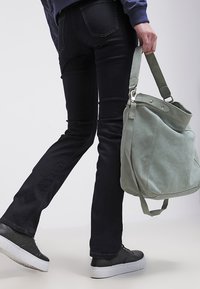 Grønn lærveske med myk tekstur og justerbar stropp, parret med mørke jeans og svarte sneakers med hvite såler.