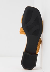 Sandale jaune à brides avec une semelle en caoutchouc noire texturée, dotée d'un talon large et de brides horizontales pour un maintien sûr.