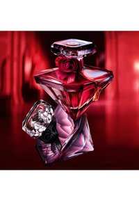 Zwei diamantförmige Parfümflaschen, eine rote mit einer roten Rose und eine violette mit einer schwarzen Rose, vor einem roten verschwommenen Hintergrund.