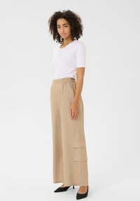 Un pantalon large beige léger doté d'une taille haute et de poches cargo ; associé à un haut blanc ajusté et des escarpins noirs pointus.