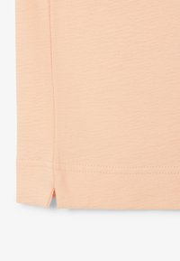 Gros plan sur un tissu couleur pêche montrant un ourlet cousu avec un petit détail d'ouverture latérale.