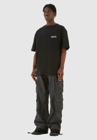 Sort oversized t-shirt med logo på brystet, parret med løstsiddende mørke cargo-bukser med flere lommer. Sorte sneakers fuldender looket.