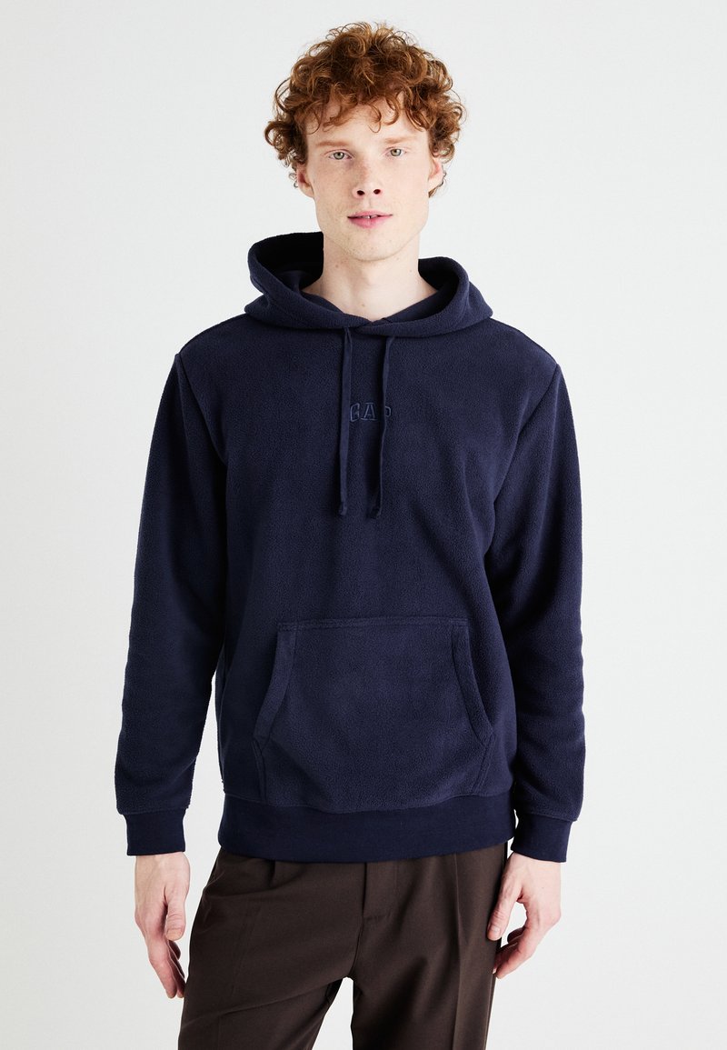 Hanorac din fleece bleumarin cu buzunar frontal, glugă cu șnur și logo brodat. Textură moale și croială lejeră.