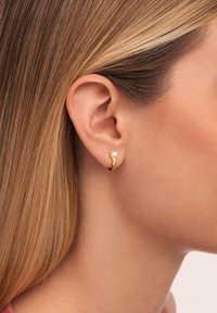 Orecchini a cerchio in oro con un design ondulato, caratterizzati da un piccolo accento di perla. Gli orecchini sono indossati da un modello, evidenziando la loro forma.