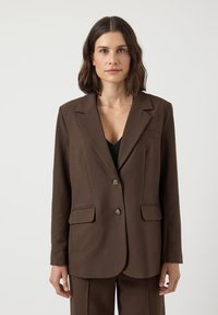 Blazer marrone realizzato in tessuto testurizzato, con revers a punta, due tasche frontali e due bottoni. Design semplice e sartoriale.
