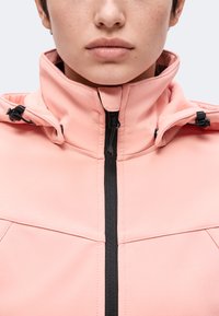 Gros plan d'une personne portant une veste rose avec un col montant et une fermeture éclair noire, montrant les lèvres, le menton et le bas du visage.