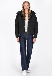 Sort pufferjakke med quiltede paneler og hætte, parret med højtaljede, mørkeblå jeans og hvide sneakers. Enkel, funktionel design.
