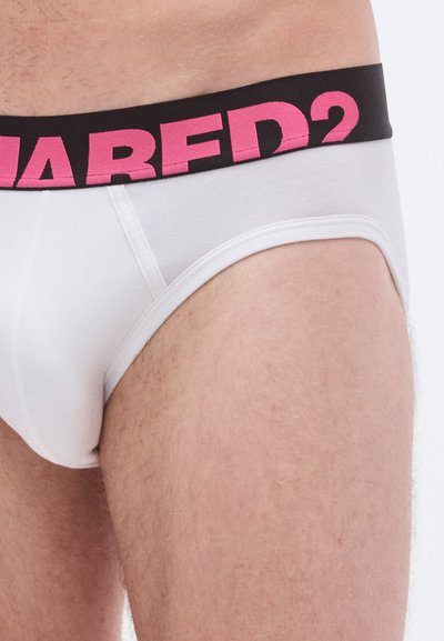 Braga blanca con cinturilla elástica negra y rosa que presenta el nombre de la marca. El material parece suave y ajustado. Mostrada sobre un muslo.