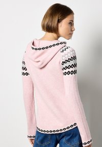 Różowy sweter z kapturem, z wzorzystymi czarno-białymi rękawami, teksturowany materiał i dekoracyjna lamówka na dole.