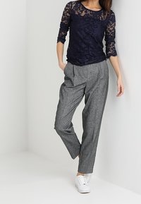 Námořnická krajková blůza s třičtvrtinovými rukávy v kombinaci se šedými přizpůsobenými kalhotami a bílými teniskami, s volným střihem a texturovaným materiálem.