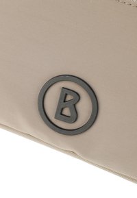 Borsa in tessuto beige con superficie testurizzata, caratterizzata da un logo circolare nero con una lettera "B" stilizzata al centro.