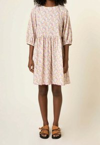 Robe à imprimé floral aux couleurs pastel claires, manches courtes bouffantes, taille froncée, ourlet festonné, assortie à des sandales marron.