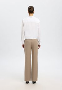 Camicia bianca con colletto e maniche lunghe, abbinata a pantaloni beige a vita alta e a gamba larga. Tacchi neri completano l'outfit.