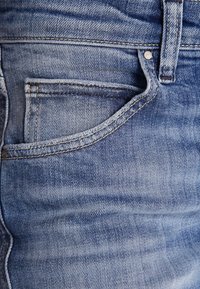 Ljusblå denimjeans med framficka, synliga sömmar och en slät textur. Tyget har ett blekt, slitet utseende.