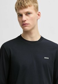 Black long-sleeve shirt made of smooth fabric, featuring a crew neck and a small white "BOSS" logo on the left chest.