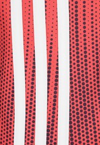 Röd tyg med svarta prickar, med tre vertikala vita ränder. Slät textur, designad för atletiska eller avslappnade plagg.