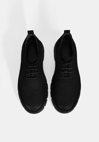 Chaussures en suède noir à lacets avec une texture lisse, bout rond et semelle en caoutchouc épaisse. Design minimaliste avec une languette.