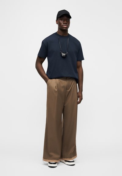 Námořnické tričko s kulatým výstřihem, volné hnědé kalhoty s širokými nohavicemi, černá čepice a černá taška na doplňky zavěšená na šňůrce. Černobílé obutí.