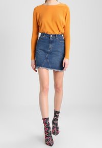Oranje geribd top met lange mouwen gecombineerd met een blauwe denim minirok met een verweerd zoom. Zwarte enkellaarsjes met bloemenpatroon maken de look compleet.