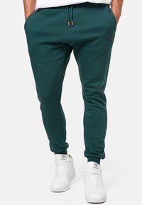 Teal jogger pants with a drawstring waistband, cuffed ankles, and a small logo detail. Made from a soft, breathable fabric.